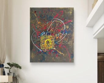May include: Abstract painting with a dark gray background and a central square of yellow, orange, and green. Splatters of red, blue, and white paint radiate outwards, creating a dynamic and colorful composition. The artwork is displayed in a modern living room.