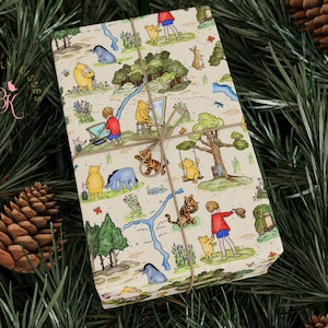 May include: Gift-wrapped package featuring a whimsical illustration of Winnie the Pooh and friends. The wrapping paper has a cream background with a repeating pattern of characters, trees, and scenes, tied with twine, set against a backdrop of pine needles and pine cones.