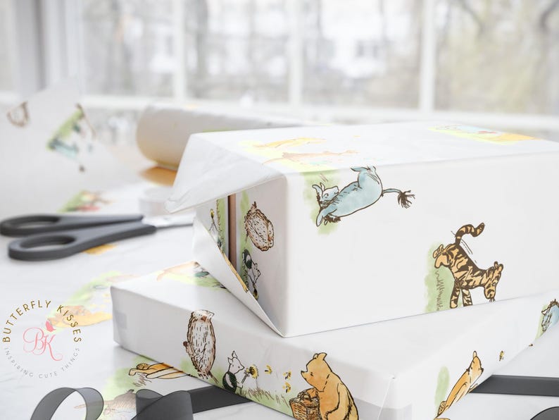 Close-up of a wrapped gift box using Classic Winnie the Pooh-themed wrapping paper, showing detailed illustrations of Pooh, Tigger, and Eeyore. The box rests on a bright white surface with scissors and tape in the background, emphasizing the paper’s smooth glossy texture and charming hand-drawn style.