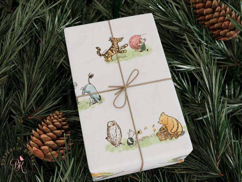 Beautifully wrapped gift in Classic Winnie the Pooh-themed wrapping paper placed among pine branches and pinecones. The hand-drawn illustrations of Pooh, Piglet, Eeyore, and Tigger evoke a nostalgic woodland holiday mood, tied neatly with rustic brown string.
