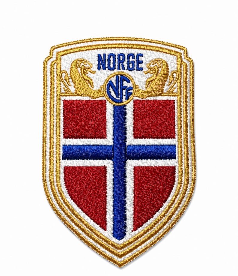 Może przedstawiać: Wyszywana naszywka w kształcie tarczy z norweską flagą w kolorach czerwonym, białym i niebieskim. Wz&oacute;r zawiera niebieski napis NORGE, okrągłe logo NFF oraz dwie złote figurki lw&oacute;w po bokach tekstu, całość wykończona złotym obszyciem.