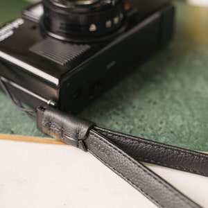 May include: A black leather camera strap with a stitched design and the word "L12" embossed on it.
