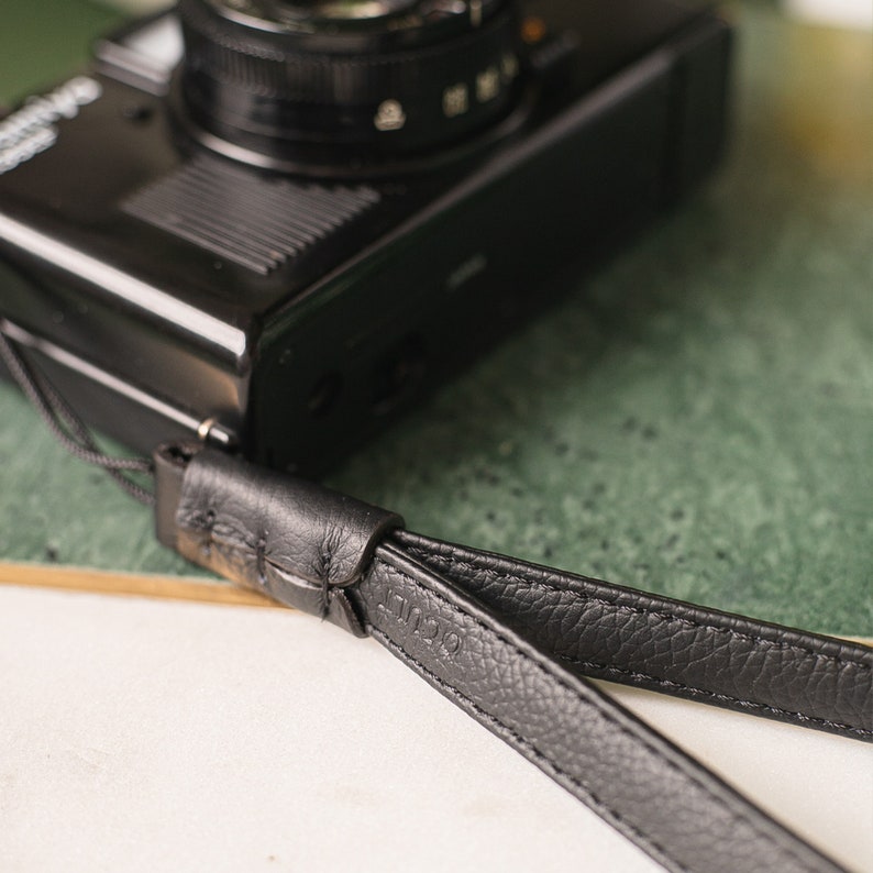 May include: A black leather camera strap with a stitched design and the word "L12" embossed on it.