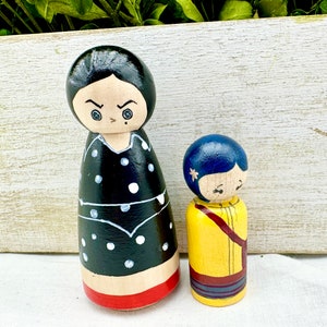 K&ouml;nnte beinhalten: Zwei Holz-Steckpuppen, eine mit schwarzen Haaren und einem schwarz-wei&szlig; gepunkteten Kleid, die andere mit blauen Haaren und einem gelben Kleid.