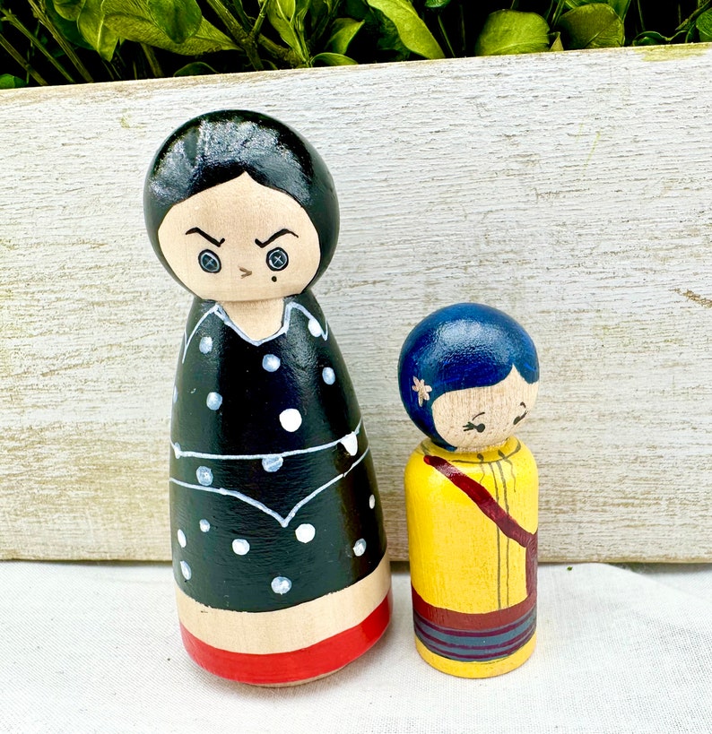 K&ouml;nnte beinhalten: Zwei Holz-Steckpuppen, eine mit schwarzen Haaren und einem schwarz-wei&szlig; gepunkteten Kleid, die andere mit blauen Haaren und einem gelben Kleid.