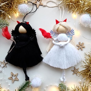 May include: Two handmade Christmas decorations, one angel and one devil, both with red horns and wings. The angel is white with silver wings and the devil is black with black wings.