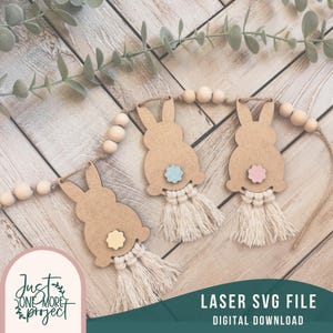 May include: A laser cut SVG file for a bunny garland with three bunnies, each with a different colored flower on its tail. The bunnies are strung together with wooden beads and twine. The text "LASER SVG FILE DIGITAL DOWNLOAD" is at the bottom of the image.