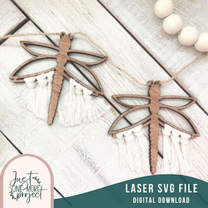 Op de afbeelding: Twee houten libellen-uitsnijdingen met witte franjes die aan een touwtje hangen. De uitsnijdingen bevinden zich op een lichte houten achtergrond. De tekst "LASER SVG FILE DIGITAL DOWNLOAD" staat onderaan de afbeelding.