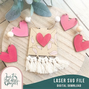 Puede incluir: Una pancarta de madera cortada con láser con un diseño de corazón y un borde de flecos. La pancarta forma parte de una guirnalda con corazones de madera y cuentas.