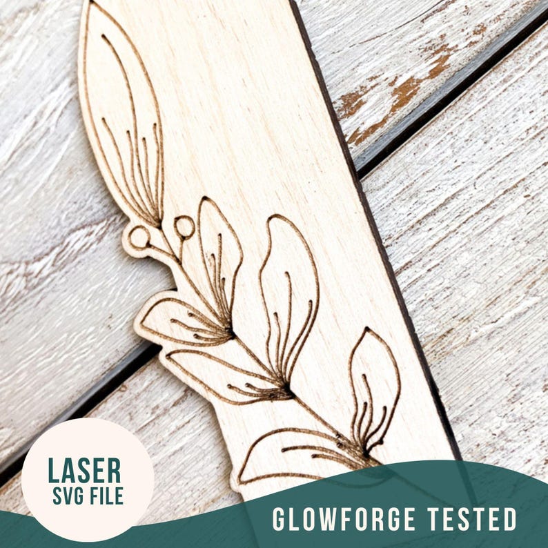 May include: A close-up of a wooden bookmark with a laser-cut floral design. The bookmark is light brown and the design is in a dark brown color. The text "LASER SVG FILE" is visible in a circle on the left side of the image. The text "GLOWFORGE TESTED" is visible in the bottom right corner of the image.