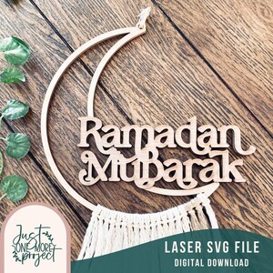 Könnte beinhalten: Holzdekor in Form eines Halbmonds mit den ausgeschnittenen Worten "Ramadan Mubarak". Das Design beinhaltet einen Makramee-Fransen und wird von einem Naturfaden gehalten. Der Text "Laser SVG File Digital Download" ist ebenfalls enthalten.