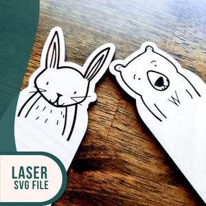 May include: Two laser cut wooden bookmarks, one with a rabbit design and the other with a bear design. Both bookmarks are white with black outlines.