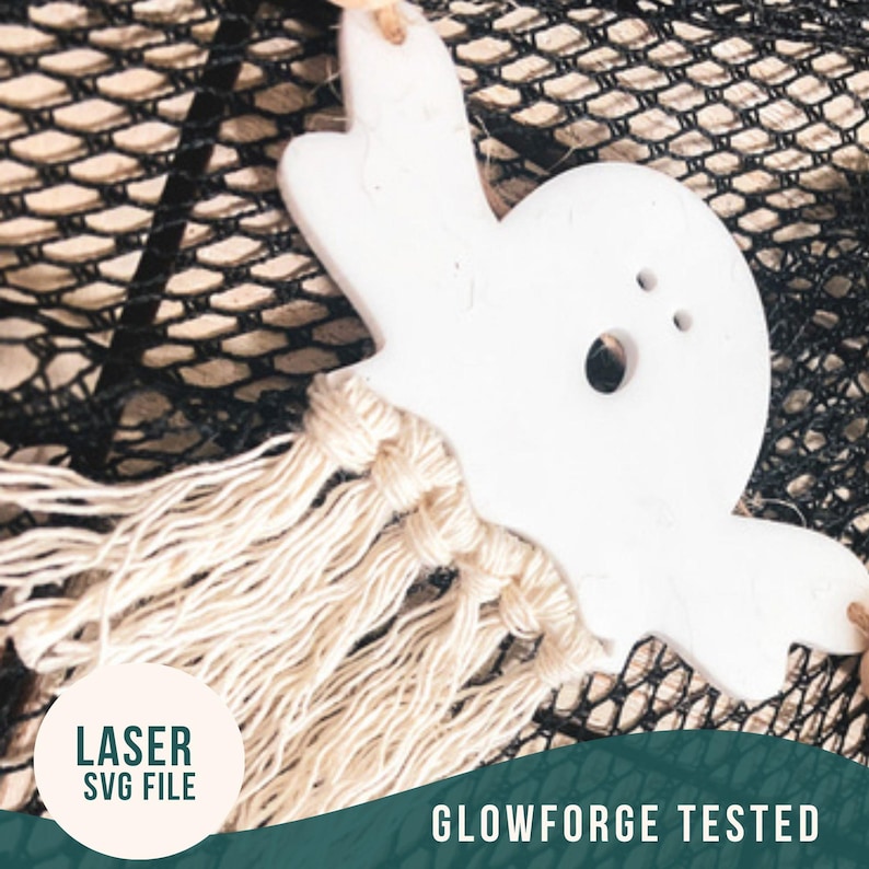 Op de afbeelding: Witte, spookvormige keramische hanger met een geknoopte franje van natuurlijke vezel die eronder hangt. De hanger bevindt zich op een zwarte gaas achtergrond. De tekst "LASER SVG FILE" en "GLOWFORGE TESTED" is zichtbaar in de afbeelding.