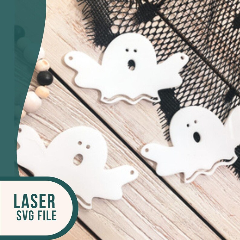 Op de afbeelding: Drie witte spookuitknipsels met een eenvoudig gezichtsontwerp. De spookjes liggen op een houten oppervlak met een zwarte kanten overlay.