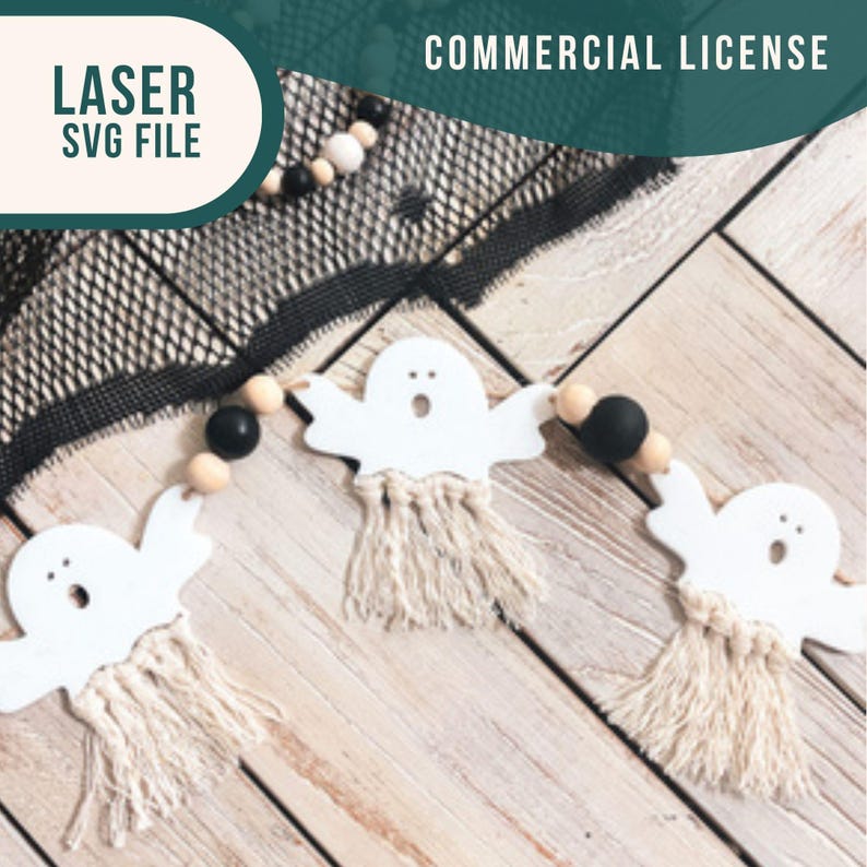 Op de afbeelding: Een witte spookengirlande met zwarte en witte kralen en een houten achtergrond. De spoken hebben franjes aan de onderkant en zijn aan elkaar geregen met touw. De tekst "LASER SVG FILE" en "COMMERCIAL LICENSE" is zichtbaar in de afbeelding.