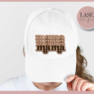 K&ouml;nnte beinhalten: Wei&szlig;e Baseballkappe mit einem braunen und schwarzen "mama"-Patch auf der Vorderseite. Der Patch hat einen Retro-Schriftart-Stil.