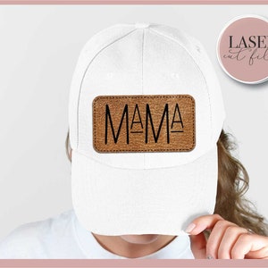 K&ouml;nnte beinhalten: Wei&szlig;e Baseballkappe mit einem braunen Lederpatch, auf dem in schwarzen Buchstaben "MAMA" steht. Der Patch hat einen gen&auml;hten Rand.
