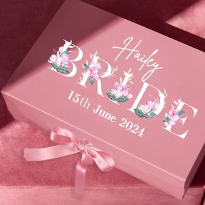 May include: Pink gift box with a white floral design and the text "Hailey Bride 15th June 2024".