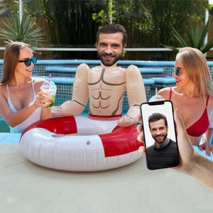 May include: A red and white inflatable pool float shaped like a life preserver with a muscular torso and head of a man. The float is in a swimming pool with two people in the background.