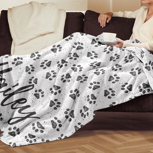 May include: White fleece throw blanket with a black paw print pattern and the name "Haley" written in black cursive script.
