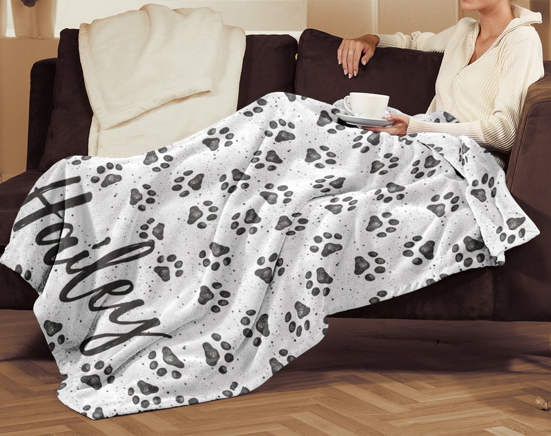 May include: White fleece throw blanket with a black paw print pattern and the name "Haley" written in black cursive script.