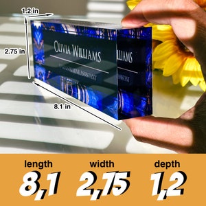 May include: A blue and gold glass desk nameplate with the text "Olivia Williams, Administrative Assistant" engraved on it. The nameplate measures 8.1 inches long, 2.75 inches wide, and 1.2 inches deep.