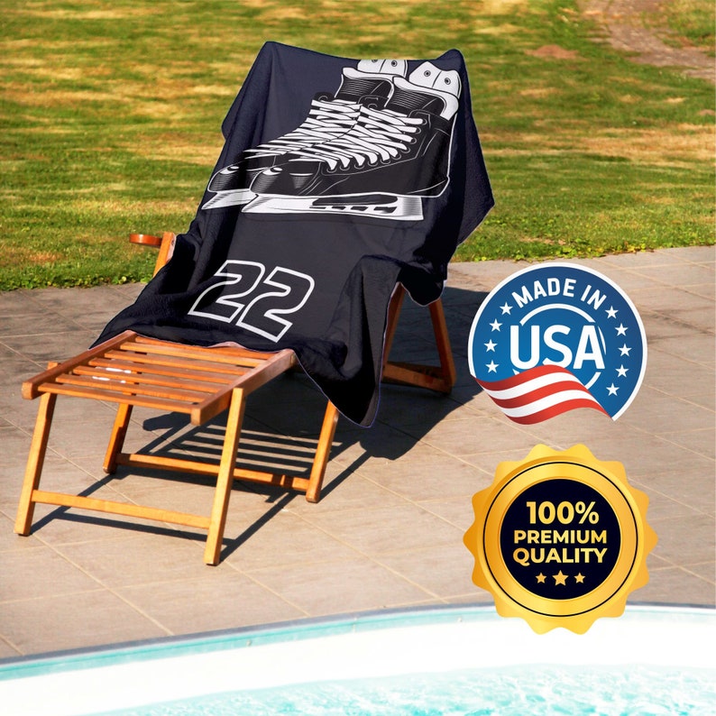 May include: A navy blue beach towel with a graphic of ice skates and the number 22 in white, draped over a wooden lounger. The towel is made in the USA and is of premium quality.