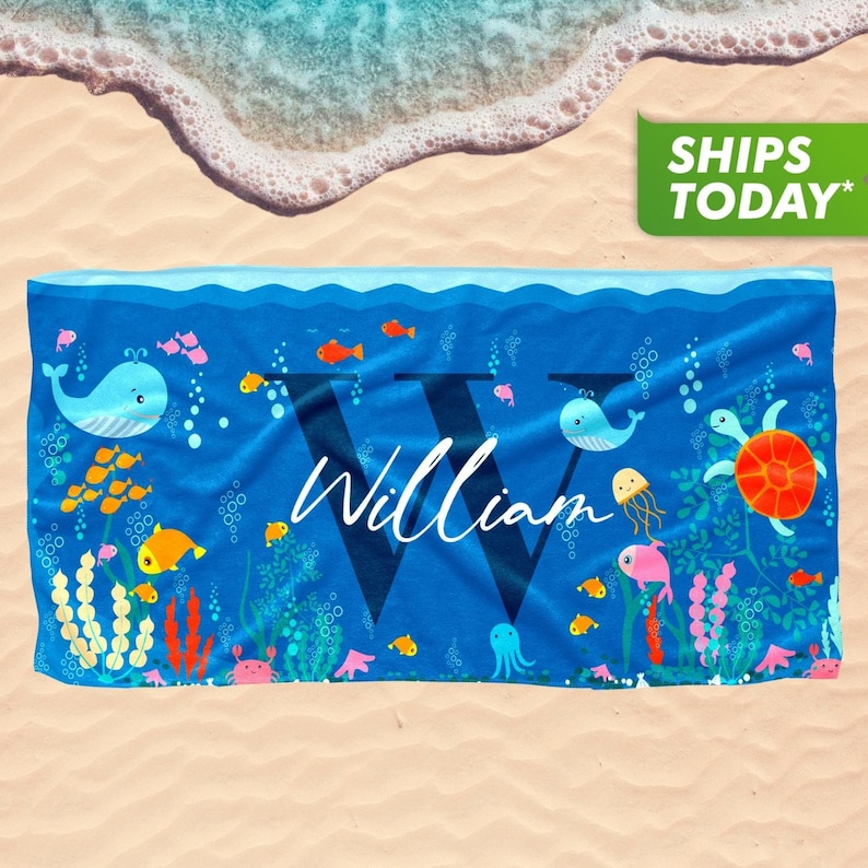May include: A blue beach towel with a large white letter "W" in the center. The letter is surrounded by colorful sea creatures, including whales, fish, and a turtle. The text "William" is written in white cursive script below the letter.