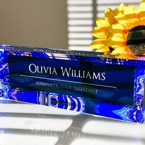 May include: A blue and white crystal desk nameplate with the text "Olivia Williams, Administrative Assistant".