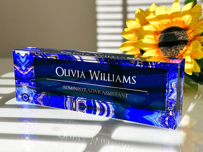 May include: A blue and white crystal desk nameplate with the text "Olivia Williams, Administrative Assistant".