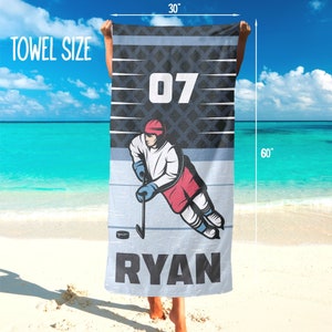 May include: A hockey-themed towel, measuring 76 cm wide and 152 cm long, with a hockey player illustration. The towel displays the number "07" and the name "RYAN". The design incorporates blue, white, and red colors.