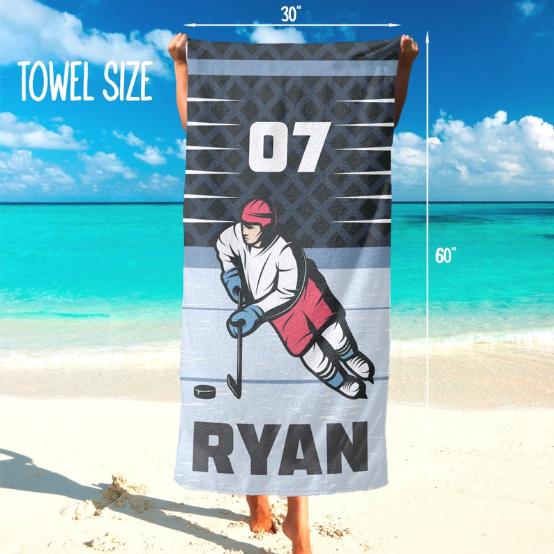 May include: A hockey-themed towel, measuring 76 cm wide and 152 cm long, with a hockey player illustration. The towel displays the number "07" and the name "RYAN". The design incorporates blue, white, and red colors.