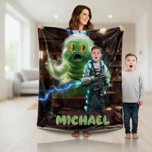 May include: A plush blanket featuring a green cartoon ghost and a boy in a costume holding a weapon. The blanket has the name "MICHAEL" in green letters at the bottom. The background shows a room with furniture.