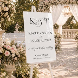 May include: A white rectangular wedding welcome sign on a wooden easel featuring black text that reads K & T, KIMBERLY NGUYEN and TAYLOR ALONSO invite you to their wedding, AUGUST 27, 2026, THREE O'CLOCK IN THE AFTERNOON in a serif font.