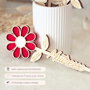 May include: A red and white flower-shaped wooden decoration with a mirror center, and a wooden leaf-shaped item with the word "Ma&icirc;tresse" in cursive. The image also shows a white vase with other wooden decorations.