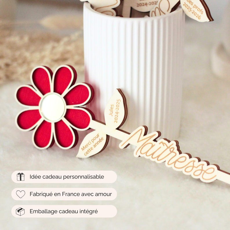 May include: A red and white flower-shaped wooden decoration with a mirror center, and a wooden leaf-shaped item with the word "Ma&icirc;tresse" in cursive. The image also shows a white vase with other wooden decorations.