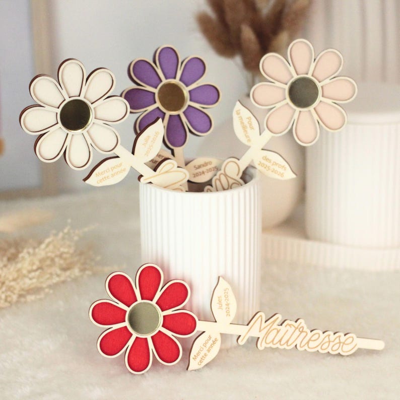 May include: Wooden flower decorations in white, purple, pink, and red. Each flower has a mirrored center and is attached to a wooden stem with a leaf. Some stems have text, including "Merci pour cette ann&eacute;e" and "Ma&icirc;tresse".