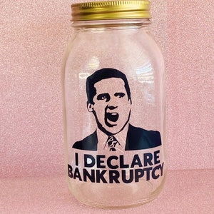 May include: A clear glass jar with a gold lid. The jar features a black and white image of a man with the text "I DECLARE BANKRUPTCY" printed on it.