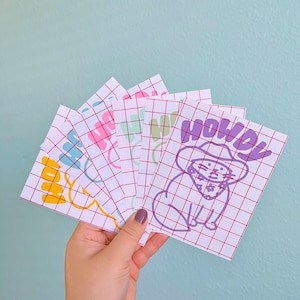May include: A set of six colorful stickers with grid patterns. The stickers feature a cartoon cat wearing a cowboy hat and the word "Howdy".