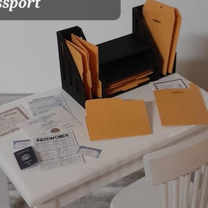 May include: Miniature office scene with a white desk, chair, and black paper holder. Includes manila folders, envelopes, documents, and a passport. The text on the image lists the items included: 2 slotted paper holders, 1 stacked paper holder, 6 manila folders, etc.