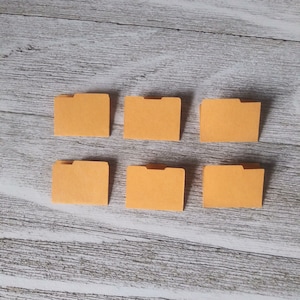 May include: Six orange file folders arranged in two rows of three on a white wood background.