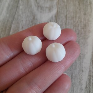 May include: Three small white ceramic pumpkins. The pumpkins are smooth and have a rounded shape.