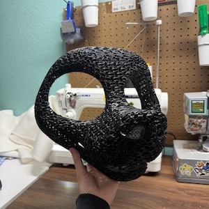 Könnte beinhalten: Eine schwarze, 3D-gedruckte Tiermaskenbasis mit einer texturierten, netzartigen Struktur, großen Augenöffnungen und einer markanten Schnauze. Die Maske hat einen hohlen Innenraum und eine abgerundete Form mit einem detaillierten, geschichteten Filamentmuster.