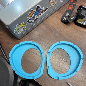 K&ouml;nnte beinhalten: Zwei identische, leuchtend blaue, kreisf&ouml;rmige 3D-gedruckte Kunststoffrahmen mit asymmetrischem Innenausschnitt und kleinen Kerben am Au&szlig;enrand. Diese Bauteile haben eine glatte, matte Oberfl&auml;che und sind mit einem erh&ouml;hten Rand versehen.
