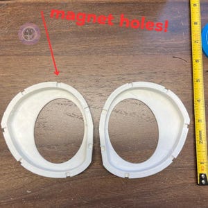 May include: Two white plastic circles with a hole in the center. The circles are labeled "magnet holes!"