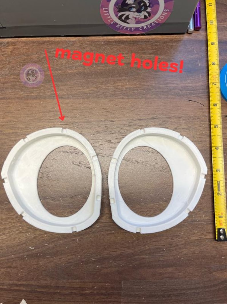 K&ouml;nnte beinhalten: Zwei wei&szlig;e, ovale Kunststoffrahmen mit gekerbten Kanten und vorgesehenen Magnetl&ouml;chern, platziert neben einem gelben Ma&szlig;band, das eine L&auml;nge von etwa 28 cm anzeigt. Der Text "magnet holes!" steht in roter Schrift &uuml;ber den Rahmen.