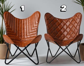 May include: Two brown leather butterfly chairs with black metal frames. Chair 1 has a geometric stitched pattern, while chair 2 features a diamond-quilted design. The chairs are set against a neutral background, with potted plants on either side.
