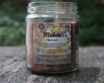 May include: A brown glass jar candle with a label that reads "White Witches Brew Mabon Ritual Candle". The label also includes text about the Autumn Equinox and the harvest.