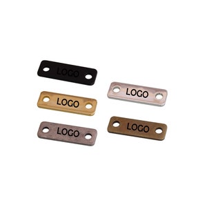 May include: Four metal tags with the word "LOGO" engraved on them. The tags are in black, gold, silver, and antique brass.