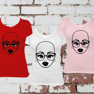 May include: Three v-neck t-shirts in red, white, and pink, each featuring a black graphic of a bald face wearing glasses and lipstick. The shirts are displayed against a brick wall background.